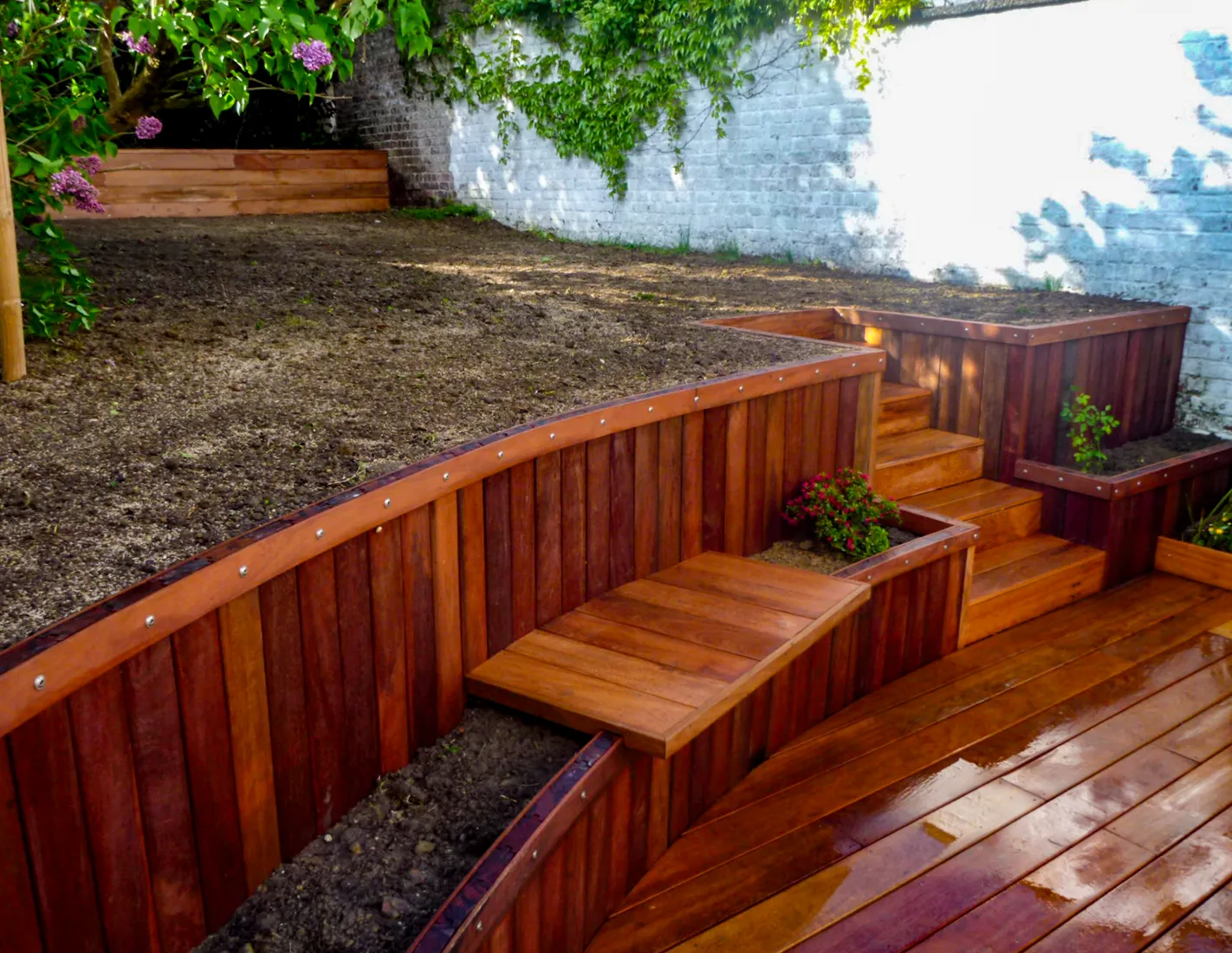 Muret de sout&egrave;nement courbe en bois exotique reliant une terrasse en bois &agrave; la pelouse