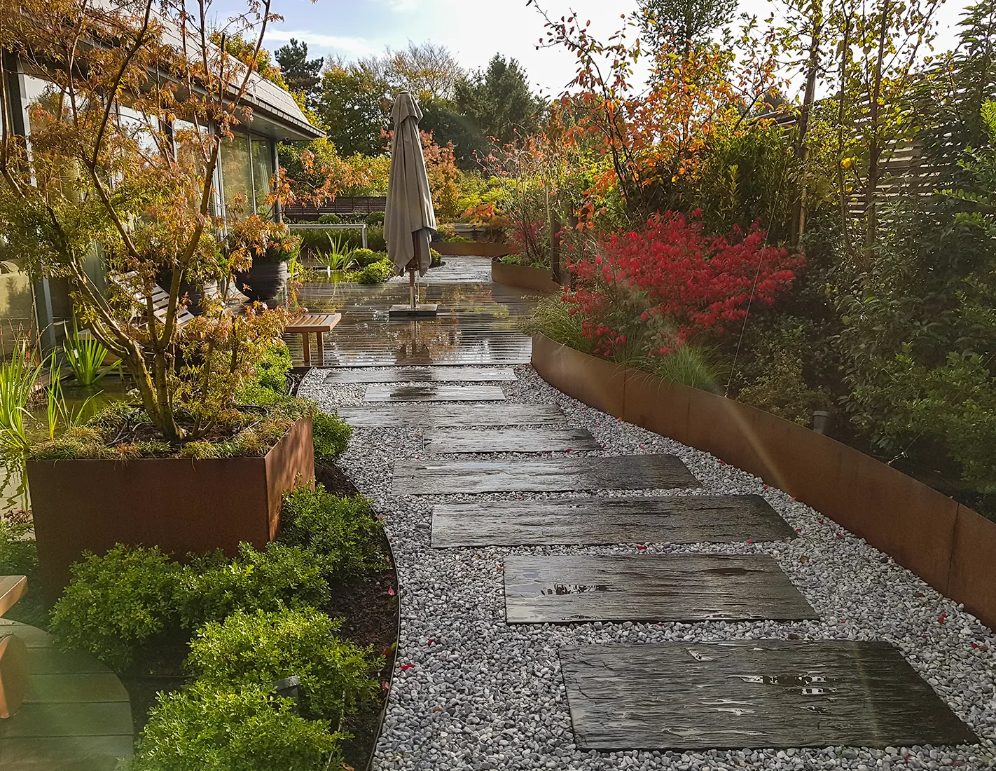 Bordure de jardin en acier corten courbe délimitant une allée de dalles sur gravier blanc