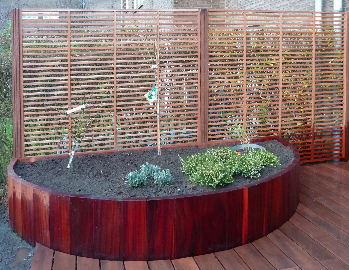 Bac de plantation semi-circulaire en palplanches arrondies d'azobé sur une terrasse en bois exotique