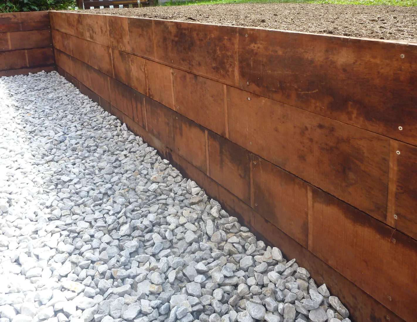 D&eacute;tail d'un muret de sout&egrave;nement en planches d'azob&eacute; &agrave; fixation viss&eacute;e apparente, avec bande de gravier drainante au pied