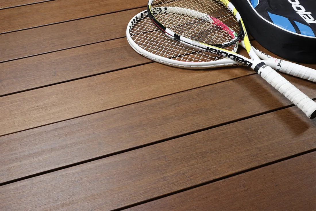 Terrasse en bambou lisse claire avec raquettes de tennis pos&eacute;es dessus