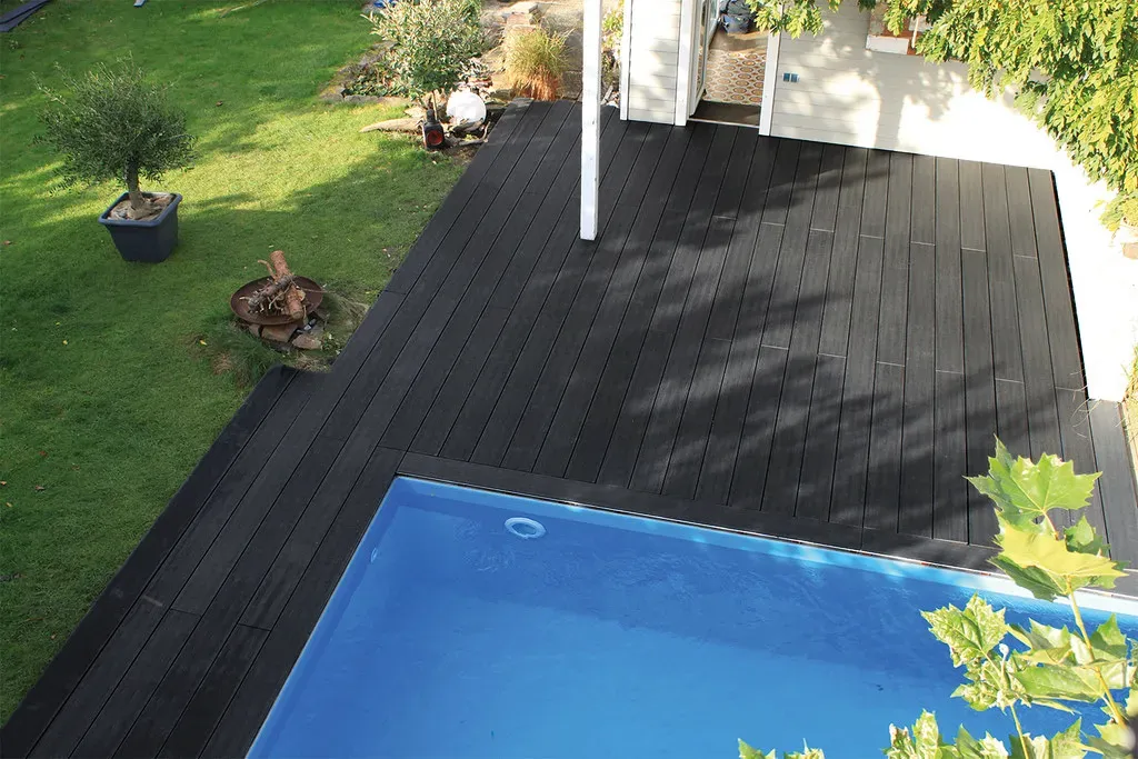 Vue en plong&eacute;e d&rsquo;une terrasse composite noir entourant une piscine dans un jardin