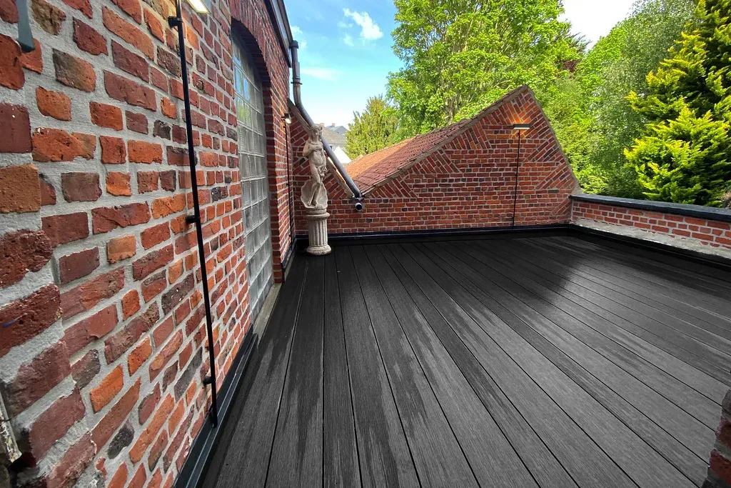 Vue en perspective d&rsquo;une terrasse en bois composite noir sur balcon, murs en briques et statue en fond