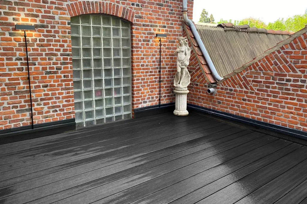 Terrasse composite noir sur balcon en briques, surface humide et reflets d&rsquo;eau